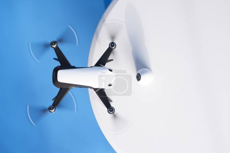 Eine komplizierte Aufnahme einer ausgeklügelten weißen Quadrocopter-Drohne mitten im Flug, die ihre High-Definition-Kamera und ihr schlankes Design vor einem kontrastierenden blauen Himmel präsentiert.