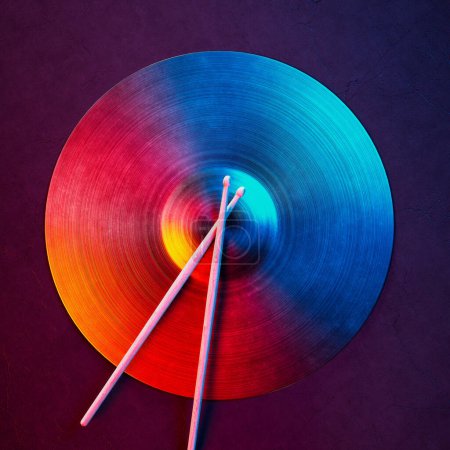 Photo for An extraordinary depiction of motion, featuring a vibrantly hued abstract vinyl record and crisscrossed drumsticks against an engaging purple backdrop, invoking a sense of rhythm and energy. - Royalty Free Image