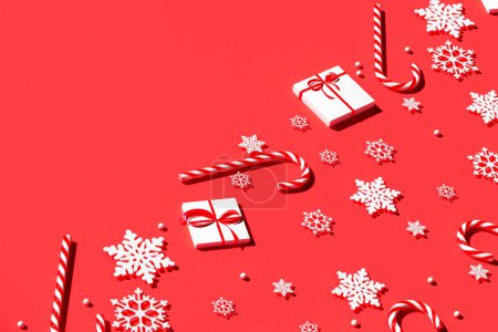 Photo for A captivating display of festive cheer with snowflakes, sweet candy canes, wrapped gift boxes, and a sprinkle of beads laid out on a stark red background for the holiday season. - Royalty Free Image