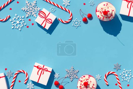 Foto de Una llamativa composición navideña sobre un telón de fondo azul que muestra regalos envueltos, bastones de caramelo a rayas, intrincados copos de nieve y un cupcake festivamente adornado. - Imagen libre de derechos