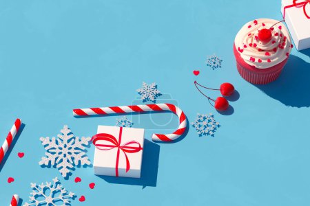 Photo for An inviting seasonal display featuring a beautifully wrapped gift, a delicately frosted cupcake, a classic candy cane, and decorative snowflakes, all set against an eye-catching blue background. - Royalty Free Image