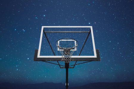 Foto de Escena nocturna cautivadora con un aro de baloncesto en silueta contra la inmensidad de un cielo nocturno estrellado, emanando un ambiente deportivo pacífico y místico. - Imagen libre de derechos