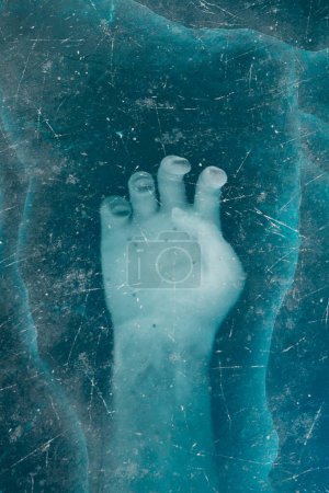Téléchargez les photos : Une capture en gros plan montre le contour d'un pied humain sous une couche de glace bleue texturée et translucide, évoquant un mélange de sérénité et de confinement.. - en image libre de droit