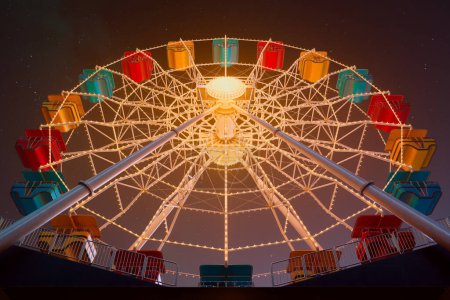 Photo for Majestic Ferris wheel bathed in multicolored lights towers against the dark sky, creating a magical scene of joy and entertainment at the nighttime amusement park. - Royalty Free Image