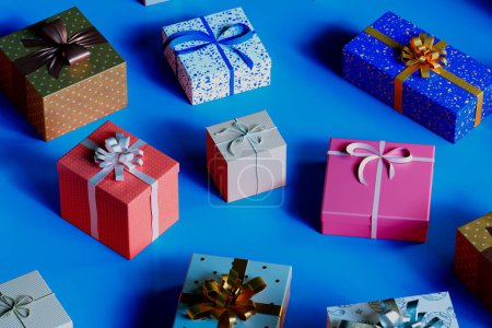 Téléchargez les photos : Un présentoir accrocheur de boîtes-cadeaux ornées de divers motifs et rubans, soigneusement disposés sur un fond bleu frappant, symbolisant la célébration et la joie. - en image libre de droit