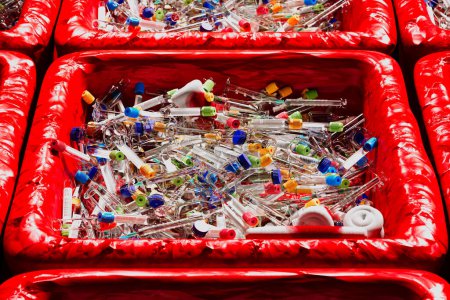 A red biohazard container overflows with discarded syringes, vials, and medical supplies, emphasizing the need for stringent waste management protocols.