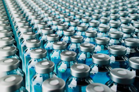 Foto de Una visión industrial expansiva de numerosas botellas de agua de plástico con tapas de plata, todas alineadas en un transportador, ejemplificando la eficiencia y la escala de la producción de agua embotellada. - Imagen libre de derechos