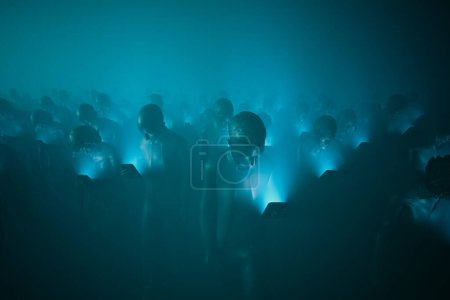 Photo for A sea of people, each bathed in the cool, blue light of personal devices, reflects our deep connection to the digital landscape, highlighting the stark contrast of technology in social settings. - Royalty Free Image