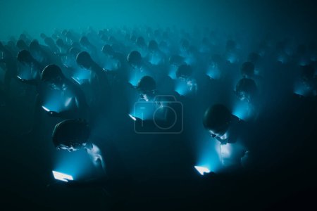 Photo for Vivid depiction of a crowd deeply absorbed in their smartphones, bathed in a monochromatic blue light that casts an otherworldly aura, symbolizing modern digital connection and isolation. - Royalty Free Image