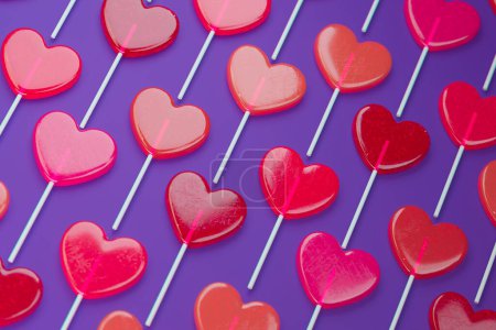 Téléchargez les photos : Tableau de sucettes rouges en forme de cœur sur une surface violette, parfait pour la Saint-Valentin, thèmes romantiques, ou occasions festives. Idéal pour l'imagerie pilotée par concept. - en image libre de droit