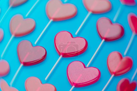Photo for Close-up view of luscious red heart lollipops symmetrically arranged against a striking blue background, symbolizing affection, joy, and festive celebrations in a sweet context. - Royalty Free Image