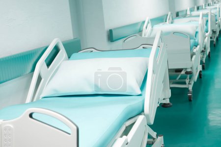 La imagen captura una fila organizada de camas de hospital vacías en un pasillo prístino, reflejando la preparación y eficiencia de las capacidades de alojamiento para pacientes del centro de atención médica..