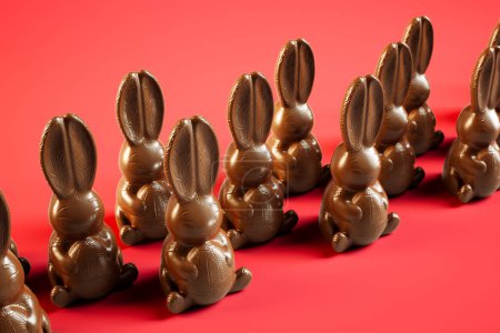 Téléchargez les photos : Délicieux lapins de Pâques au chocolat méticuleusement alignés sur un fond rouge audacieux, incarnant l'indulgence traditionnelle des fêtes et les festivités de Pâques joyeuses. - en image libre de droit