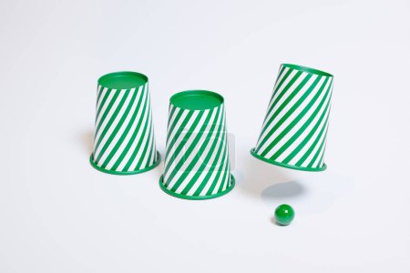 Foto de Vibrantes copas de rayas verdes y blancas volteadas al lado de una bola a juego en blanco, lo que significa el intrigante juego de conchas. Perfecto para conceptos de azar, habilidad e ilusión. - Imagen libre de derechos