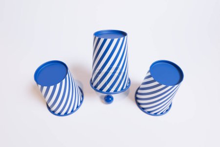 An aesthetically pleasing arrangement of three blue and white striped ceramic cups overturned with a coordinating ball, set against a stark white background to enhance visual impact.