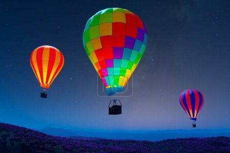 Téléchargez les photos : Un trio de montgolfières lumineuses dérive élégamment sur un champ parsemé de fleurs, sous la toile captivante d'un ciel nocturne étoilé, symbolisant liberté et rêves.. - en image libre de droit