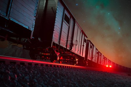 Téléchargez les photos : Une image saisissante capture un train de marchandises stationnaire baigné dans les feux rouges du crépuscule, sur fond de ciel nocturne incrusté d'étoiles, représentant le transport et l'aventure. - en image libre de droit