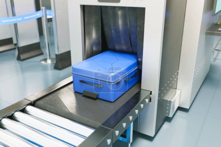Close-up view of a striking blue suitcase placed on a conveyor belt at an airport security checkpoint, symbolizing contemporary travel safety procedures and checks.
