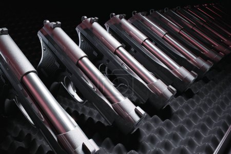 Mehrere Handfeuerwaffen in makelloser Anordnung vor dunklem, strukturiertem Hintergrund, die eine organisierte Kollektion mit starkem Schwerpunkt auf Symmetrie und Präzision präsentieren.