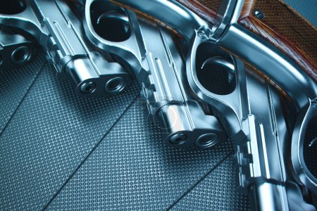 Foto de Imagen capturada por expertos que destaca los revólveres gemelos con empuñaduras de madera, colocados sobre un robusto telón de fondo metálico oscurecido, enfatizando la complejidad del diseño de armas de fuego. - Imagen libre de derechos