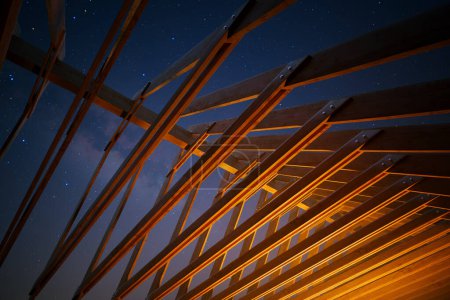 Foto de Surge un enigmático edificio de madera, bañado en calor por sus brillantes luces bajo el amplio tapiz de una noche llena de estrellas, evocando asombro y serenidad. - Imagen libre de derechos
