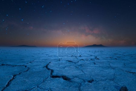 Téléchargez les photos : Un spectacle spectaculaire de la nuit étoilée cosmique descendant habilement sur le paysage désertique fissuré et stérile, avec les derniers chuchotements du crépuscule à l'horizon. - en image libre de droit