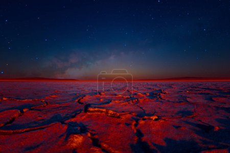 Foto de Majestuosa noche se despliega sobre un vasto desierto, donde el terreno crujido brilla bajo un impresionante tapiz de estrellas brillantemente centelleantes. - Imagen libre de derechos