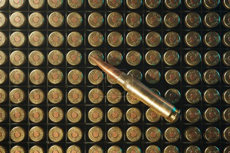 A solitary rifle bullet lies diagonally across a meticulously arranged backdrop of gleaming, unfired cartridges, encapsulating a potent symbol of armament.