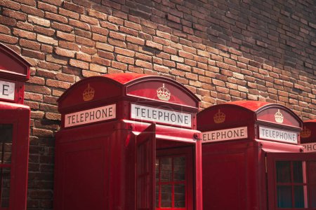 Foto de Una escena británica por excelencia capturada con una fila de icónicas cabinas telefónicas rojas, mostrando su diseño atemporal junto a una pared de ladrillo rústico bajo la suave luz del sol. - Imagen libre de derechos