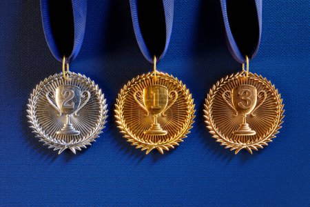 Photo for The distinct sheen of gold, silver, and bronze medals against a royal blue fabric highlights recognition and the spirit of competitive excellence. Ideal for representing rankings in any event. - Royalty Free Image