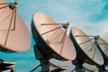Una gama dinámica de antenas parabólicas blancas se elevan hacia el cielo azul claro, simbolizando la vanguardia de las tecnologías mundiales de telecomunicaciones y transferencia de datos.