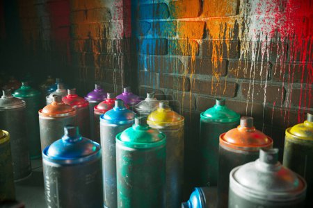 Photo for Utilized spray paint cans lie scattered with lids askew against the backdrop of a graffitied urban brick wall, exemplifying the raw essence and colorful vibrance of street art. - Royalty Free Image