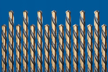 Photo for A meticulously arranged selection of golden drill bits lay on a striking blue surface, embodying precision, contrast, and engineering excellence in a close-up view. - Royalty Free Image