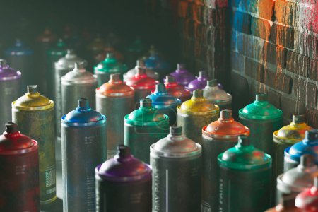 Photo for An elaborate array of multi-hued spray paint cans positioned against a textured brick wall backdrop, showcasing a palette of tools indicative of urban street art and creativity. - Royalty Free Image