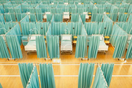 An aerial shot captures a well-ordered temporary hospital setup featuring multiple beds partitioned with teal privacy curtains, precisely arranged for efficient mass patient care.