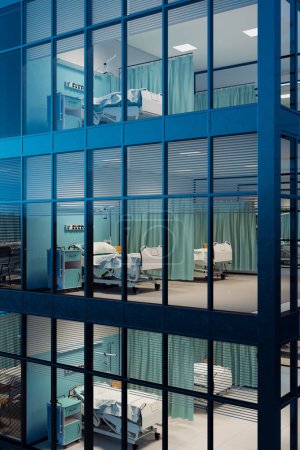 Eine ruhige und beschauliche Szene, die eine Krankenhausstation bei Nacht einfängt, mit leeren Betten und medizinischen Werkzeugen, wie man sie durch reflektierende, blau getönte Glasfenster sieht..