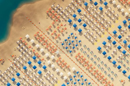 Diese atemberaubende Luftaufnahme zeigt eine lebhafte Strandszene, in der ein Teppich aus bunten Sonnenschirmen einen wunderschönen Kontrast zum klaren türkisfarbenen Wasser und dem weißen Sandstrand bildet..