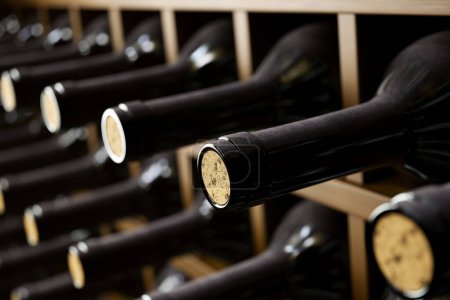 Téléchargez les photos : Une vue détaillée des bouteilles de vin premium avec des bouchons visibles soigneusement alignés dans un élégant rack en bois, mettant en valeur une collection de vins sophistiqués dans un cadre de cave traditionnelle. - en image libre de droit