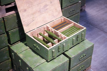 Une caisse en bois ouverte montre des munitions militaires soigneusement disposées, adjacentes à des boîtes de rangement en métal vert uniformes dans un environnement contrôlé et à haute sécurité..