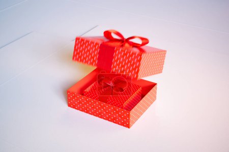 Photo for An enticing open red gift box with white polka dots and a satin ribbon, revealing a nested box inside, set on a pristine white background, symbolizing surprise and celebration. - Royalty Free Image