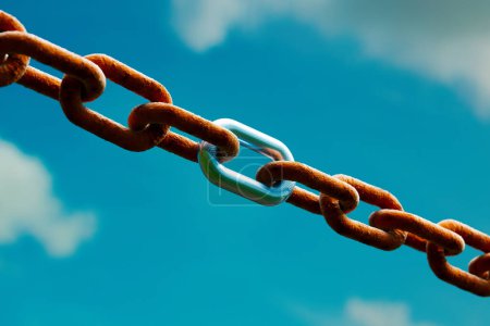A stark contrast is captured in this close-up photograph featuring rusted and glossy chain links intertwined, symbolizing endurance and renewal, set against a vivid blue backdrop.