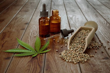 Hochwertiges Hanföl in Tropfflaschen in der Nähe von Hanfsamen und grünem Blatt auf rustikalem Holz, das natürliche Bio-Wellness und CBD-Produkte präsentiert.