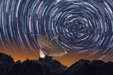 Foto de Fotografía de larga exposición que muestra una antena parabólica contra el ballet celestial de los senderos estelares en los cielos nocturnos, simbolizando la intersección de la tecnología humana y el cosmos. - Imagen libre de derechos