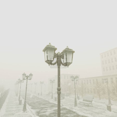 This captivating winter photograph showcases a snow-covered urban park path, with serene mist enveloping street lamps and benches during the quiet of dawn.