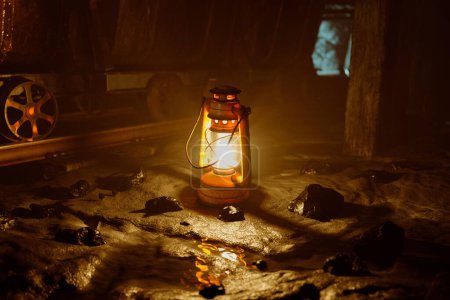 Téléchargez les photos : Une lanterne singulière à l'ancienne projette une lueur chaude et dorée dans l'obscurité enveloppante, soulignant les profondeurs intrigantes d'une mine historique. - en image libre de droit