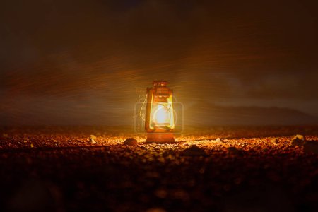 Téléchargez les photos : Une scène évocatrice comme une lanterne vintage baigne les rochers environnants dans une lumière douce et chaude sous le crépuscule de rassemblement, créant une aura de solitude paisible. - en image libre de droit