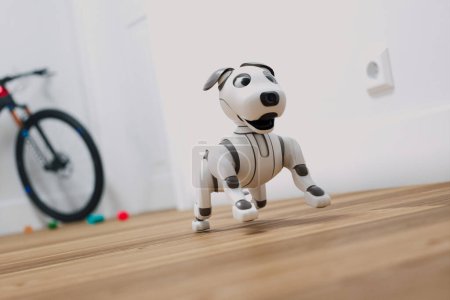 Photo for An interactive robotic dog toy, poised attentively amidst vibrant colored marbles on a sleek hardwood floor, with a child's bicycle subtly visible in the distance. - Royalty Free Image