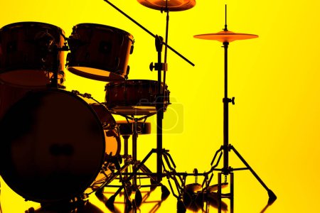 Téléchargez les photos : Une silhouette captivante d'un ensemble complet de tambours, avec des collets, des toms et des cymbales, radicalement contrasté avec un fond jaune monochrome, parfait pour les visuels sur le thème de la musique. - en image libre de droit