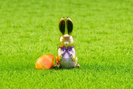 Photo for A glossy, metallic Easter bunny alongside a vividly painted egg nestled in lush green artificial grass, symbolizing the joy and tradition of spring festivities. - Royalty Free Image