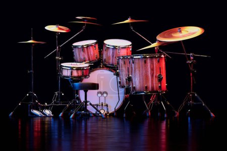 An expansive drum kit with various drums, cymbals, and drumsticks, all under moody stage lighting ready for a dynamic musical performance or studio recording.